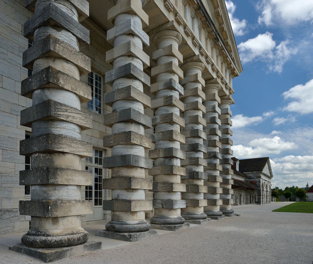 A close oblique view looks along six massive stone columns built from alternating smooth round drums and projecting square blocks beneath a heavy classical entablature.