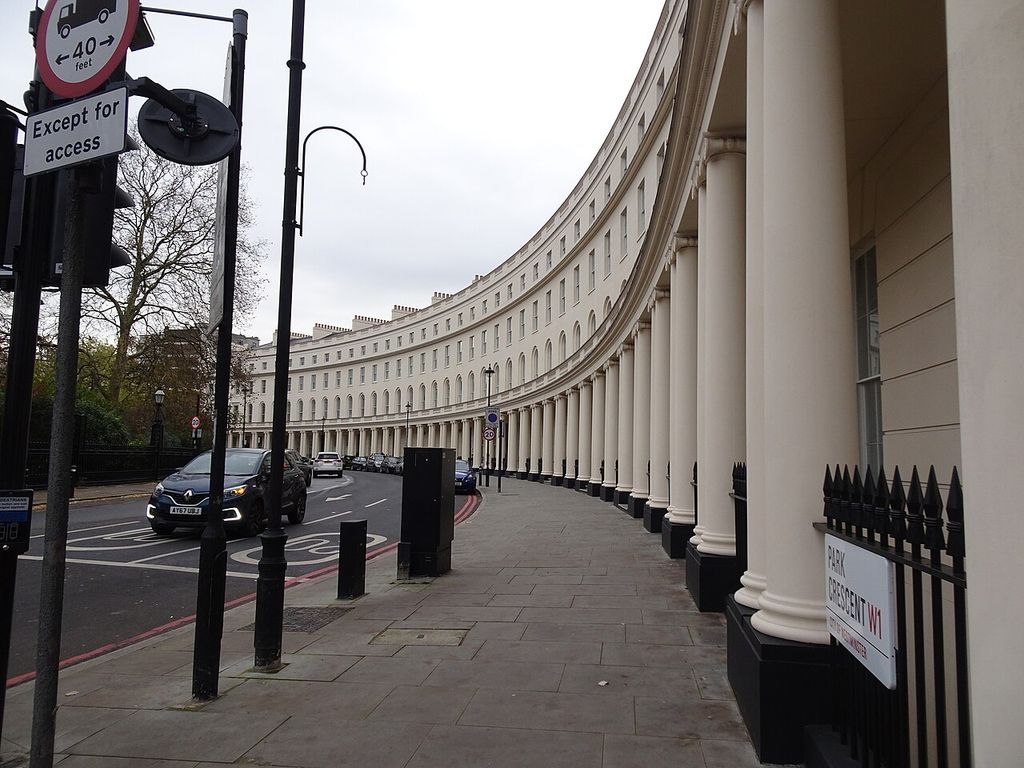 A long white crescent of repeated windows and columns curves away along a London street lined with cars, signs, lamps and black railings.