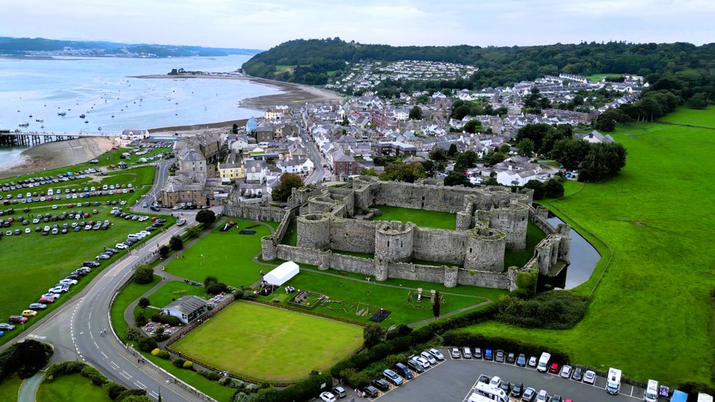 A high inner enclosure and lower outer walls surround courts beside a moat, town and coastline.