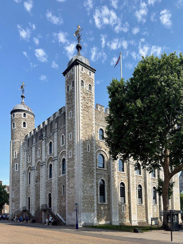 A massive rectangular stone keep with corner turrets rises within a larger historic complex.
