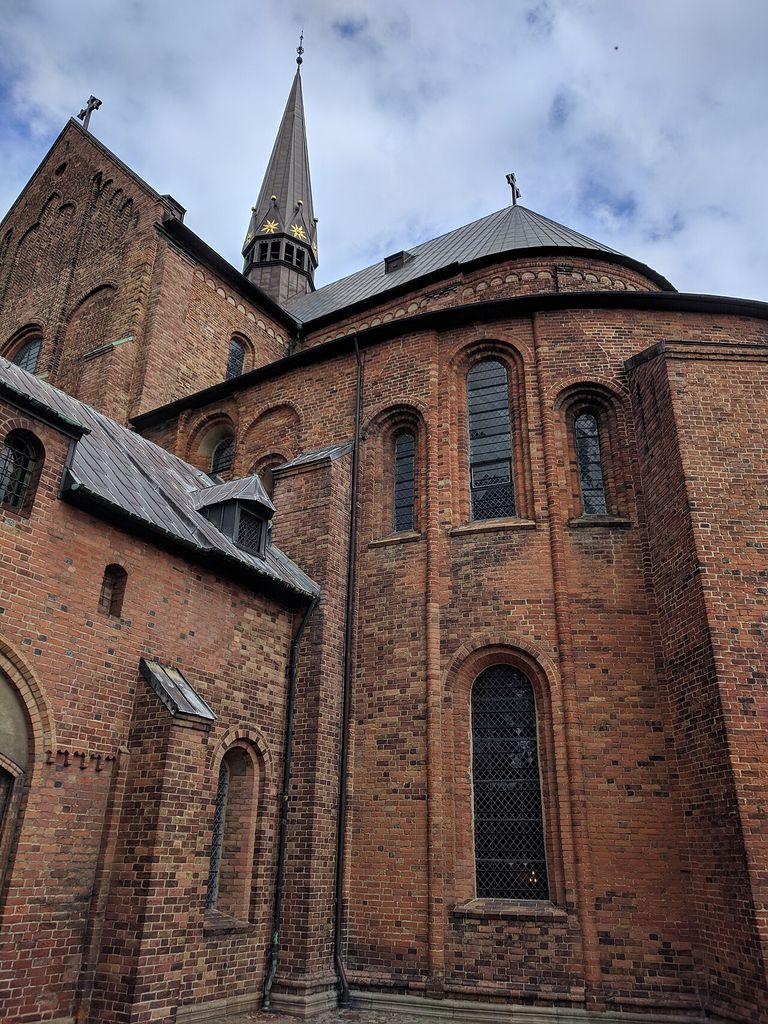 Red brick walls curve around a roofed volume with tall round-headed windows and narrow vertical projections.