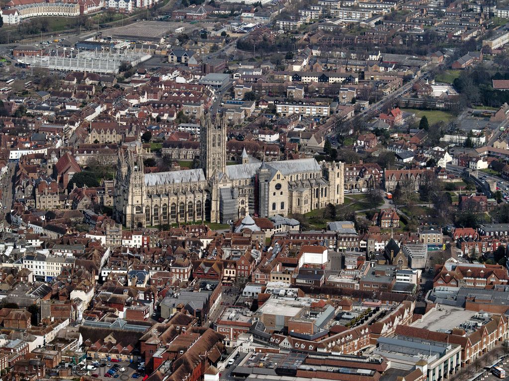 An oblique aerial view places the cathedral's long nave, west and central towers, eastern volumes and partly hidden precinct among dense streets and buildings.