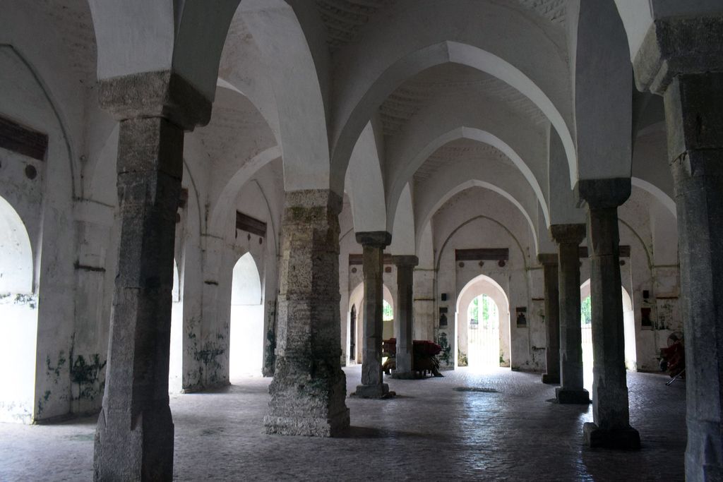 Thick dark columns divide a whitewashed prayer hall into repeated pointed-arch bays beneath small domical vaults lit from side openings.