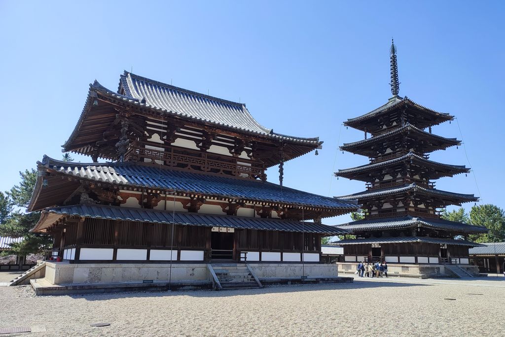 A broad timber main hall and a five-storey pagoda with layered tiled roofs stand side by side across a gravel courtyard.