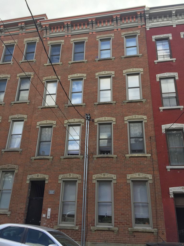 Four storeys of narrow brick façades have repeated tall windows, projecting stone heads and bracketed cornices, crossed by utility wires.