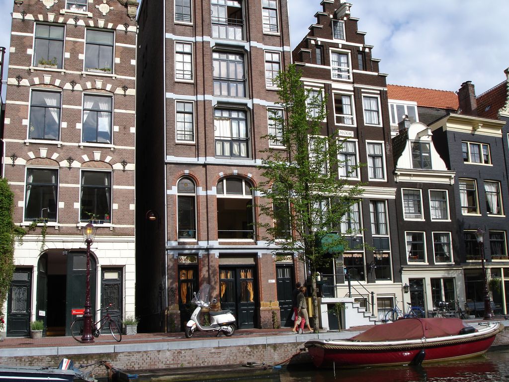 A canal-side row contains narrow brick houses with stepped and curved gables, ranked windows, shopfronts, bicycles and a moored boat.