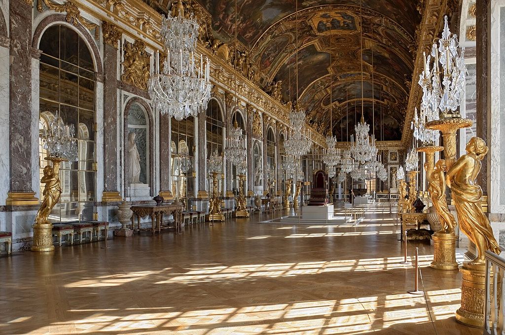 A long gilded gallery repeats mirrored arches, chandeliers and tall windows beneath a painted barrel vault.