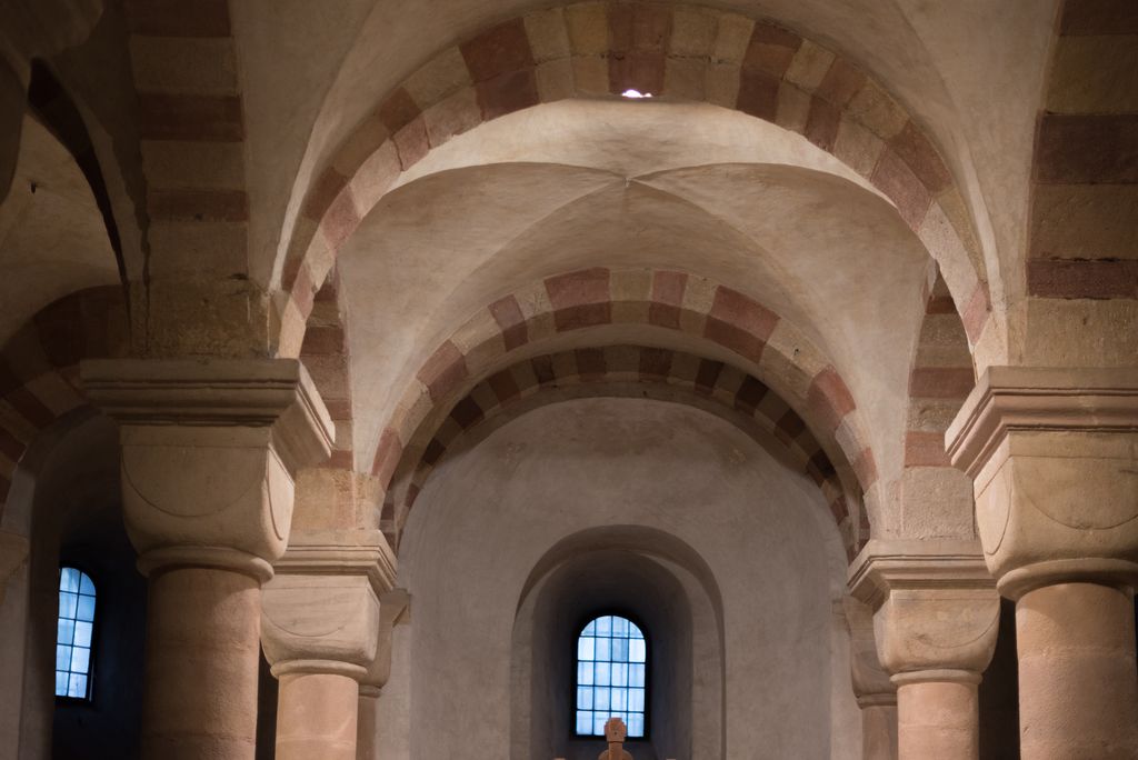 Smooth vault surfaces intersect above cushion capitals between striped rounded arches.
