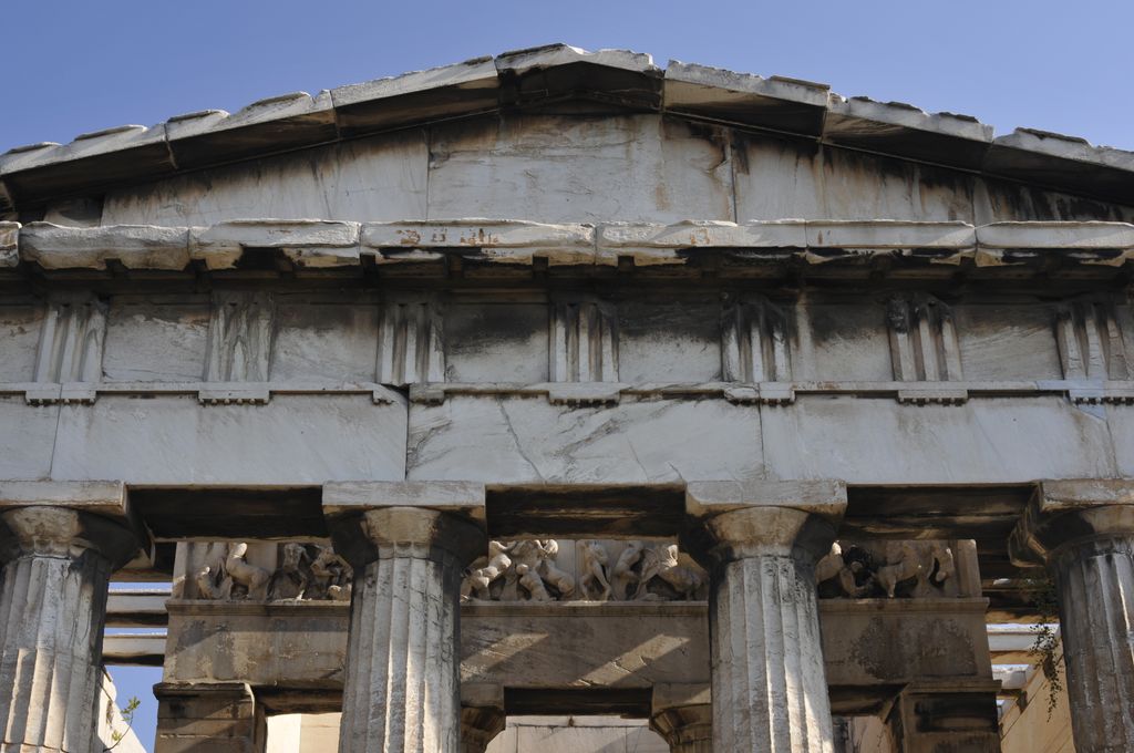 Fluted upper shafts and broad plain capitals support a stone architrave and alternating grooved triglyphs and square metopes below a pediment.