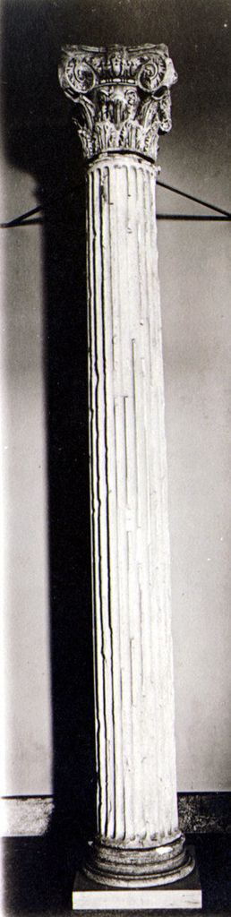 A tall fluted marble shaft rises from a moulded base to a capital combining large upper scrolls and lower leaves.