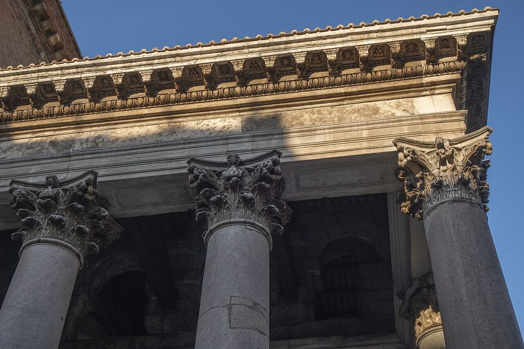 Three deeply carved Corinthian capitals top smooth grey granite shafts below a richly moulded stone entablature.