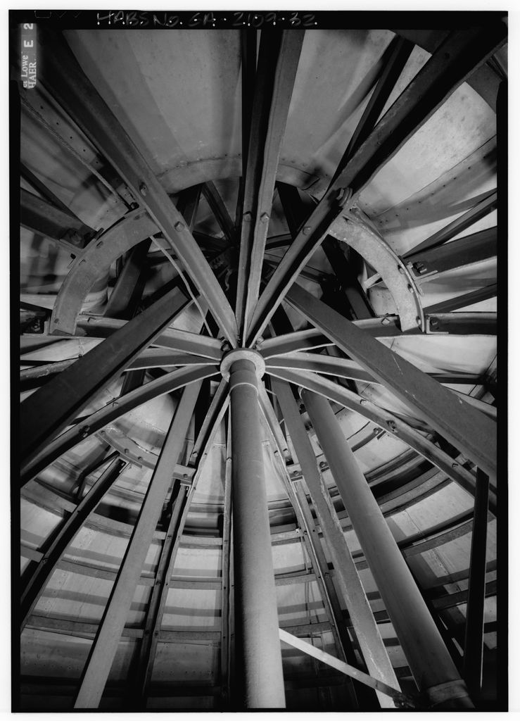 A monochrome interior view shows a circular steel ring, radial and diagonal members, central post and the inner skin of a dome.