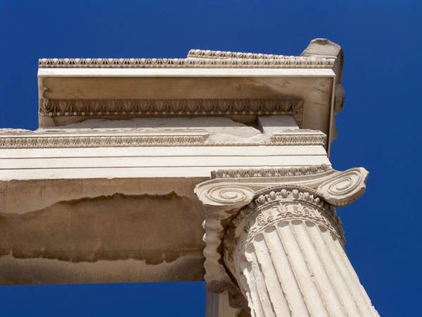 A large spiral Ionic capital tops a fluted shaft beneath several carved and projecting horizontal stone bands.