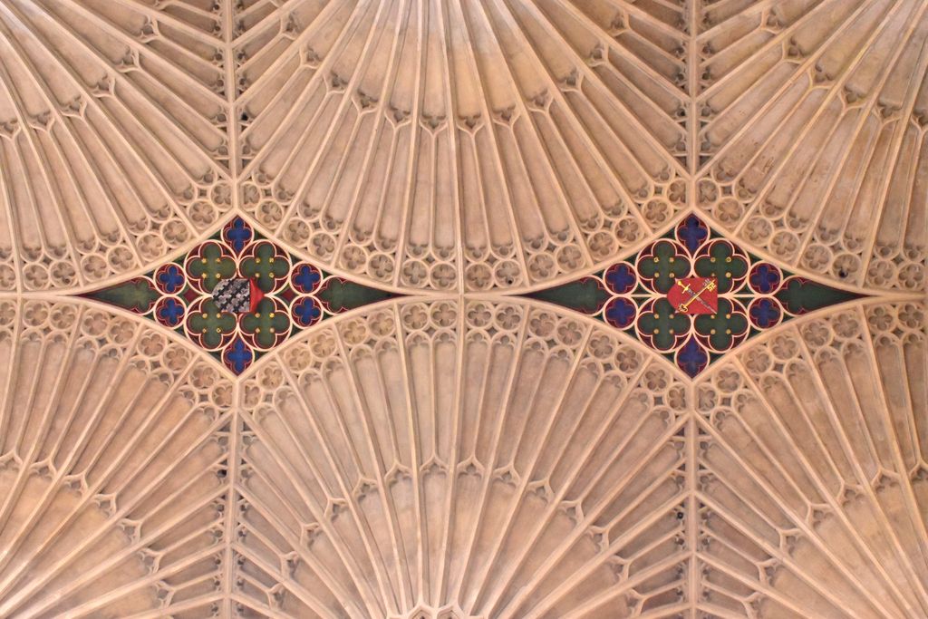 Four pale fan-shaped rib patterns meet around two coloured lozenges decorated with flowers and heraldic shields.