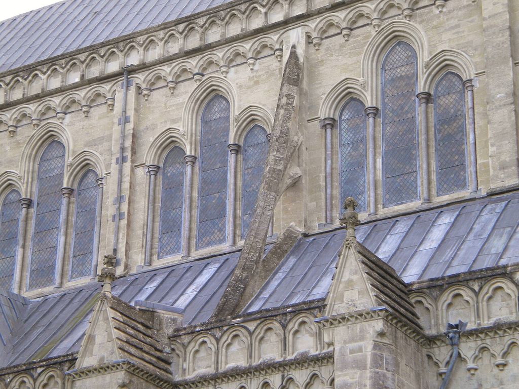 Narrow stone flyers project above a lead-covered lower roof toward the tall window wall.