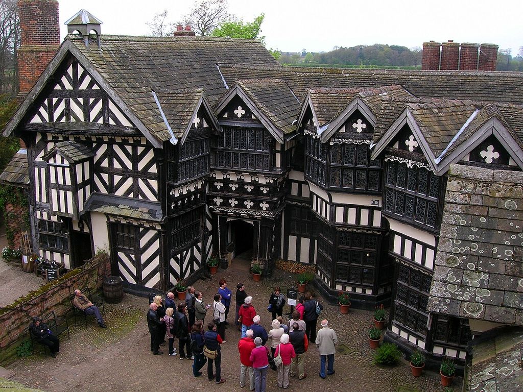 Black-and-white timber-framed ranges crowd around a cobbled court beneath several tiled gables and projecting glazed bays.