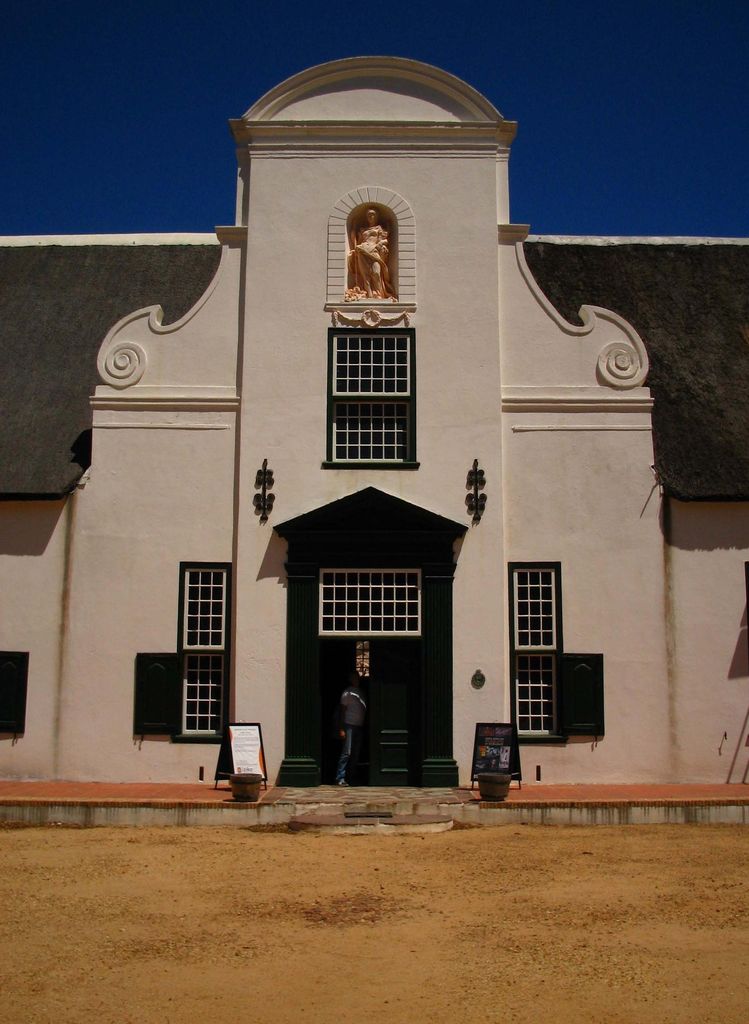 A tall white plastered centre gable with curved shoulders, scrolls, an upper niche and ranked windows rises before a dark thatched roof.