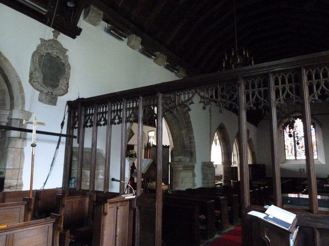 A dark timber screen of slender posts and repeated pointed tracery separates the nave from the chancel of a small white-walled church.