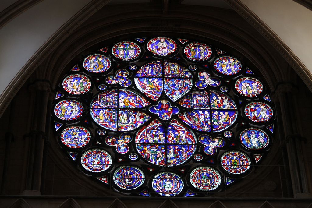 A circular stained-glass window contains broad figurative lobes, coloured perimeter medallions and small foils within a dark stone ring.