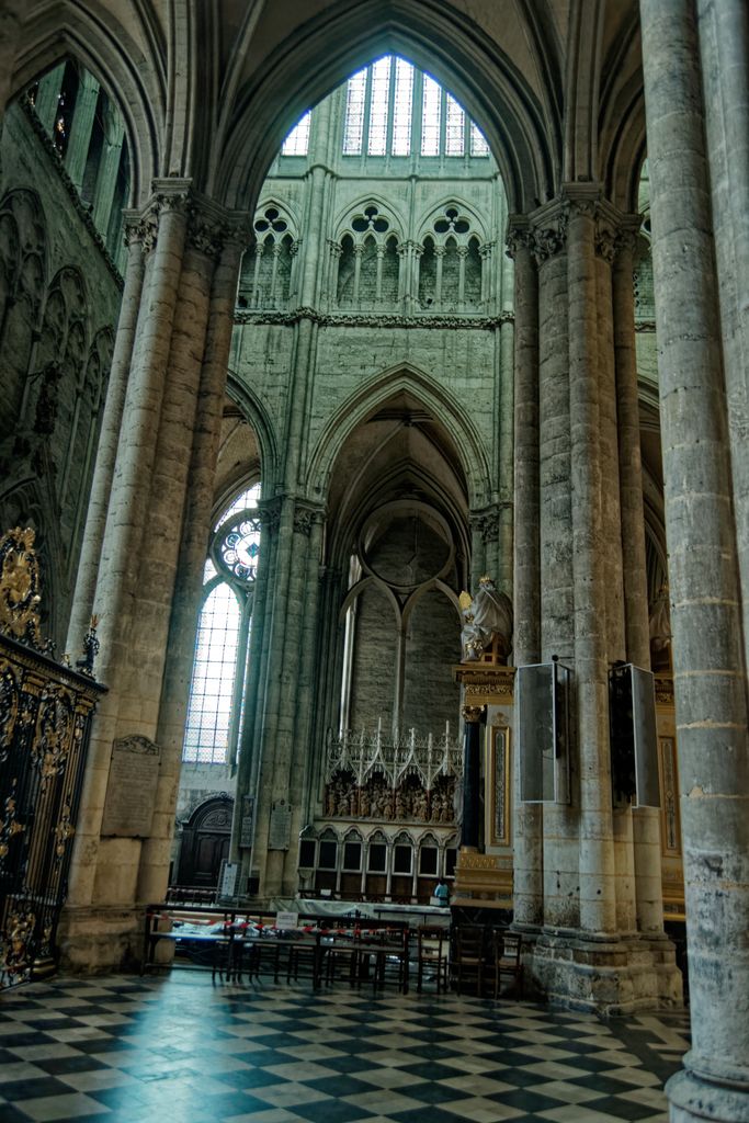 Tall pointed arches frame a transept wall with a large upper window, smaller foiled openings, slender columns and a side rose.