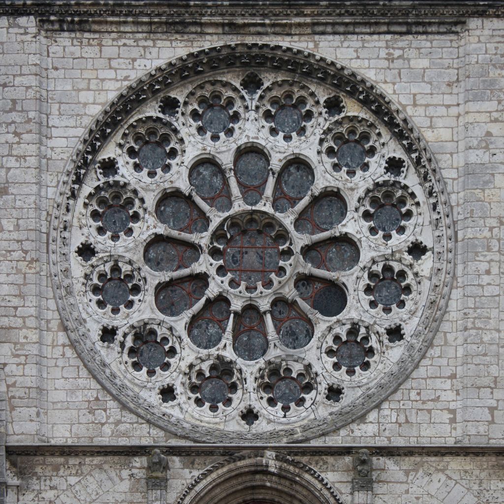 A circular window is pierced into a broad pale stone field, with rings of foiled openings around a central glazed circle.