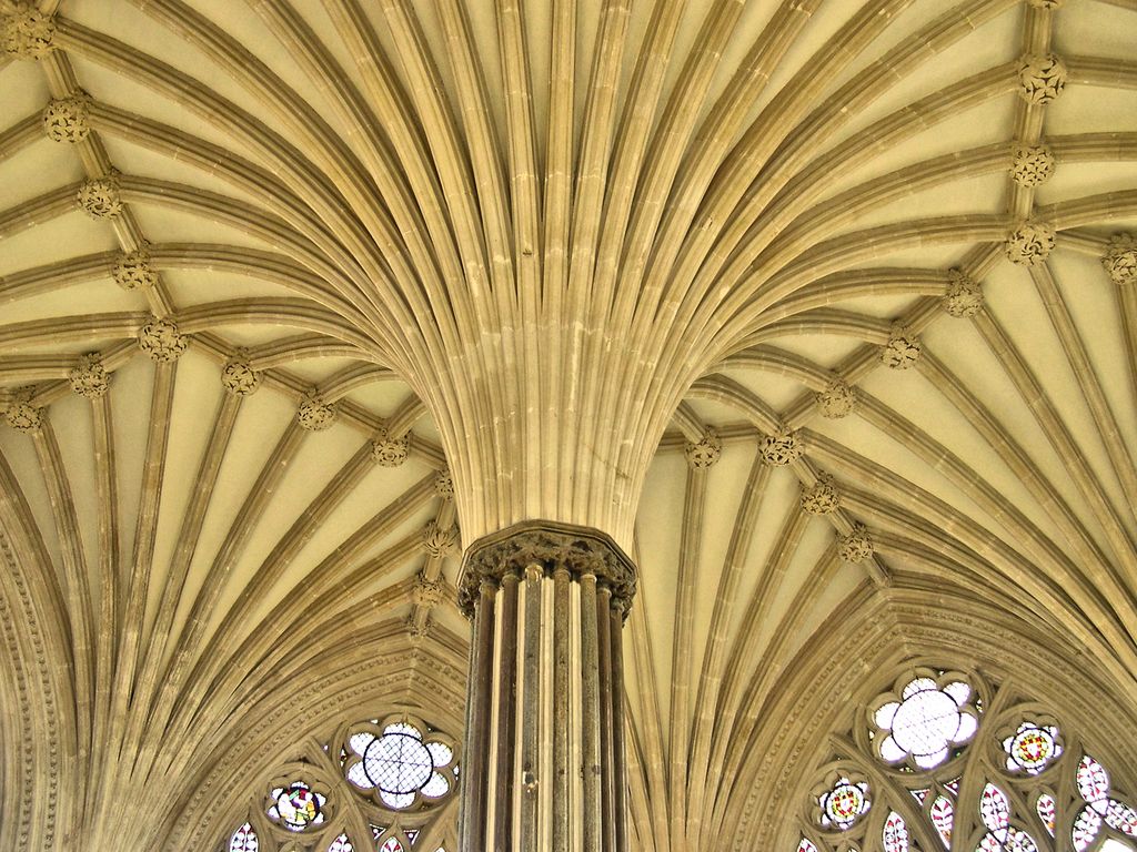 Many moulded stone ribs fan outward from the top of a central clustered pier toward carved bosses across a pale ceiling.