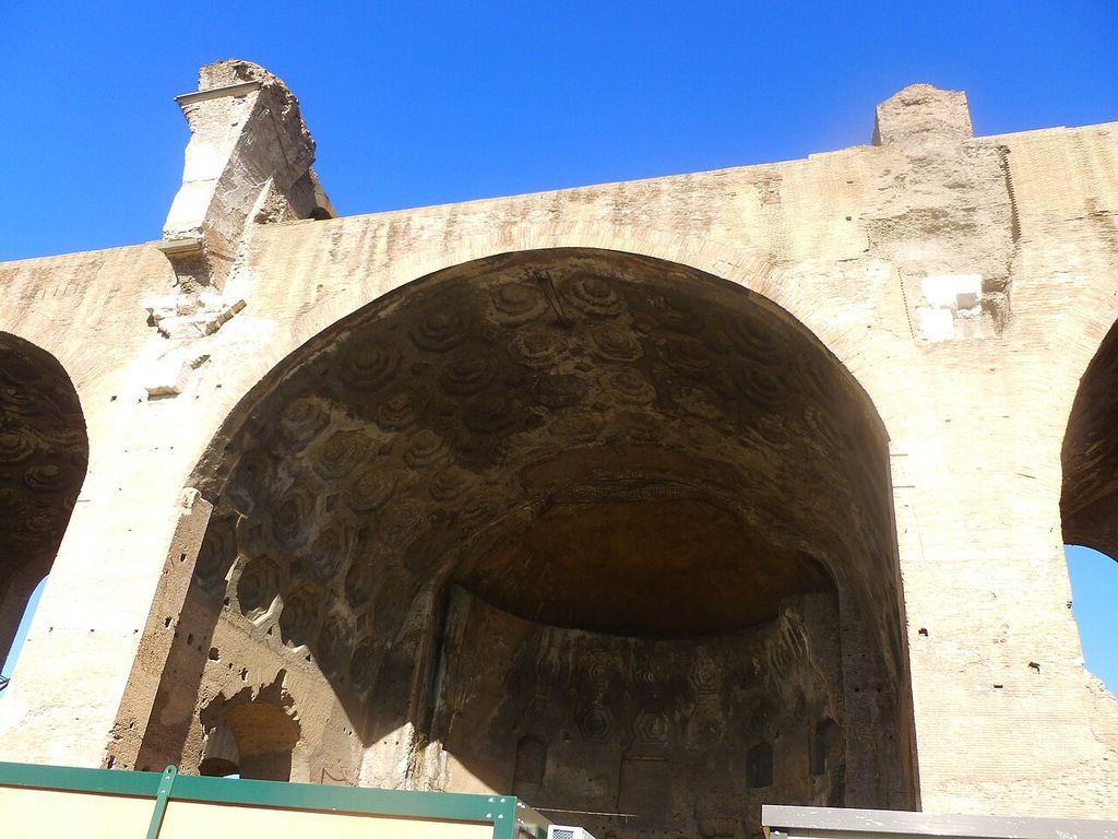 A huge coffered curved vault survives between massive masonry walls beside ruined openings.