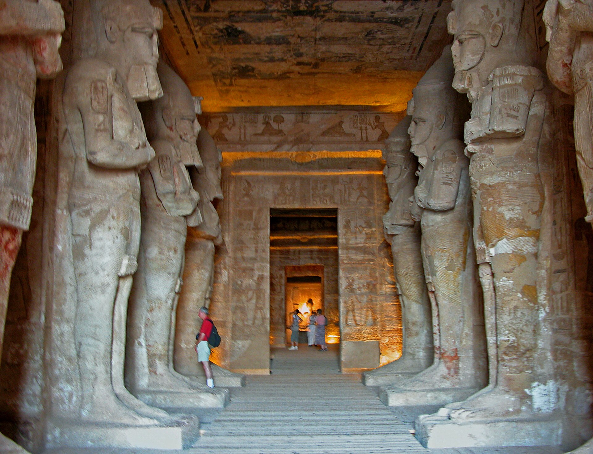 Interior axial view between two rows of four Osiride Ramesses pillar fronts, with several aligned doorways and present wooden flooring.