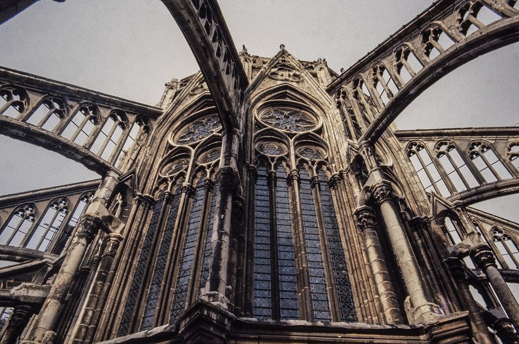 Openwork stone flying arches cross above large traceried choir windows in a grainy upward roof-level photograph of a cathedral chevet.