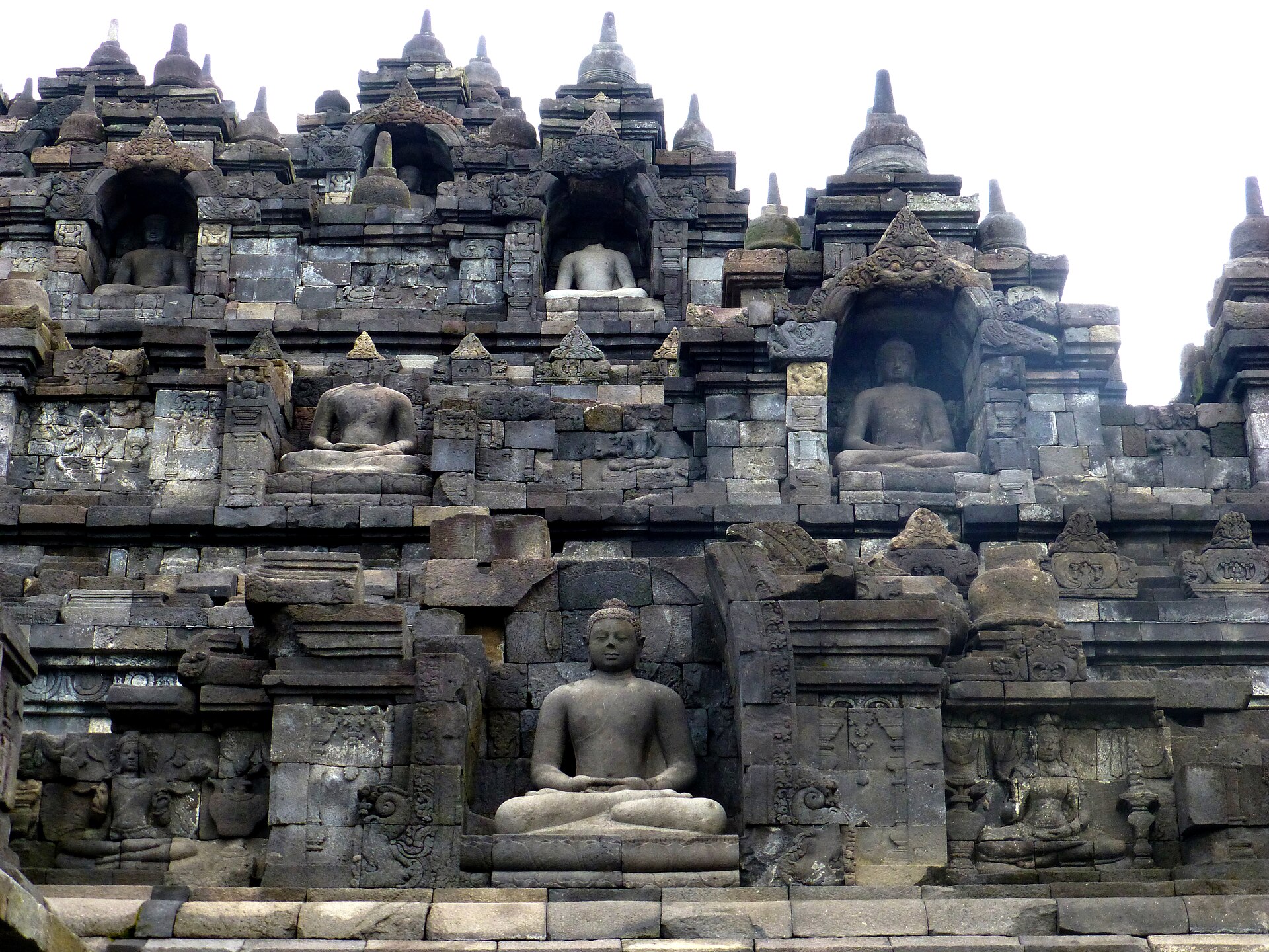 A Borobudur Buddha seated with hands joined in meditation within an ornamented stone niche, with further niches above.