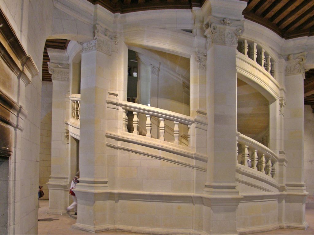 Pale stone stair flights curve behind large open arches and balustrades, with visitors visible on different levels.