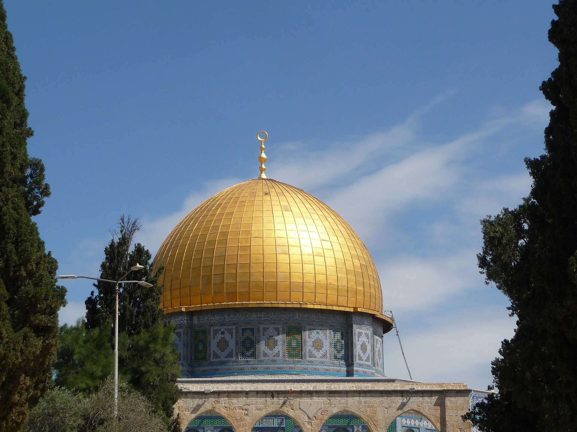 Present gold-coloured dome above the blue tiled drum and platform arcade, with trees flanking the view.