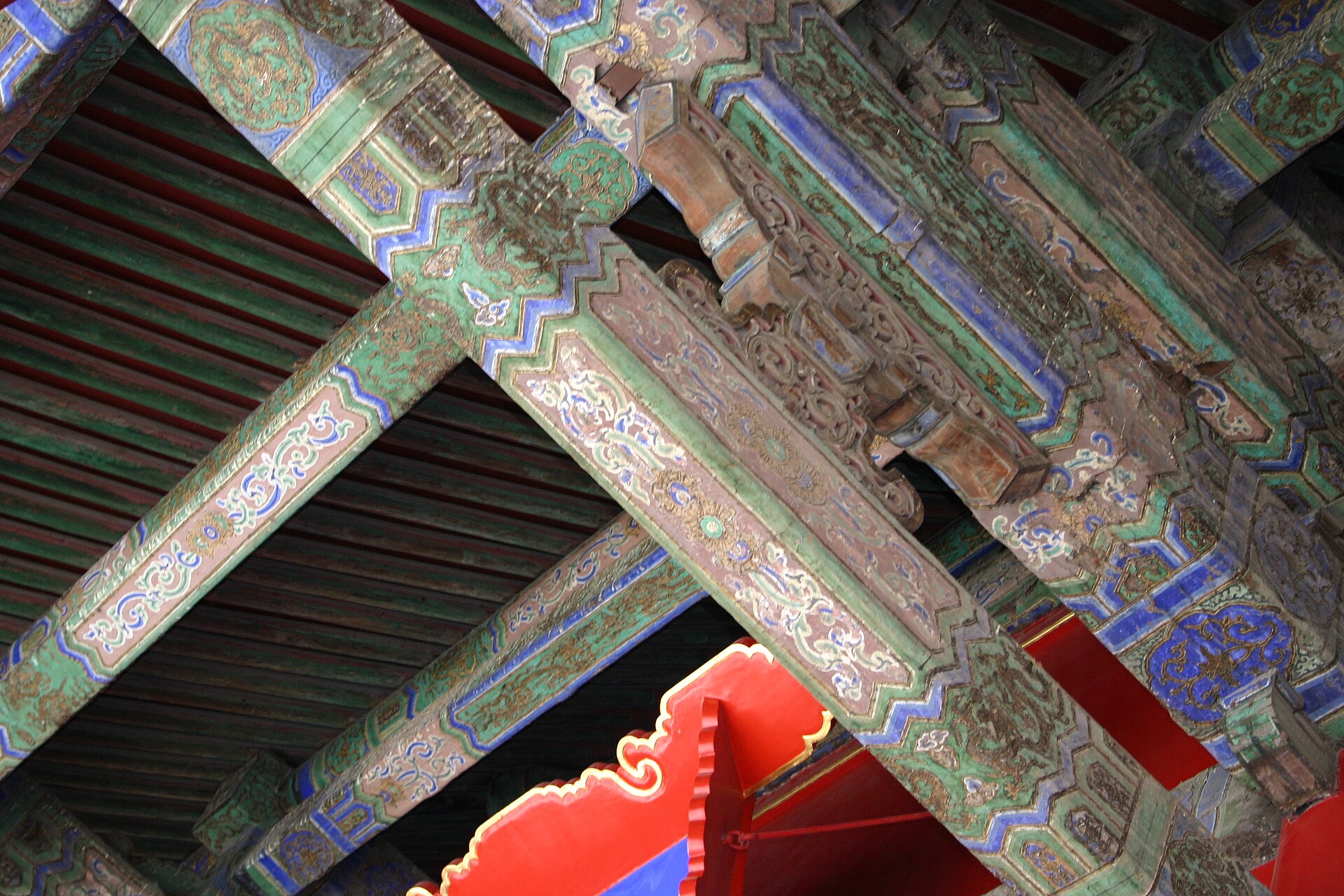 Close view up into intersecting painted beams and interlocking wooden brackets below a palace roof.