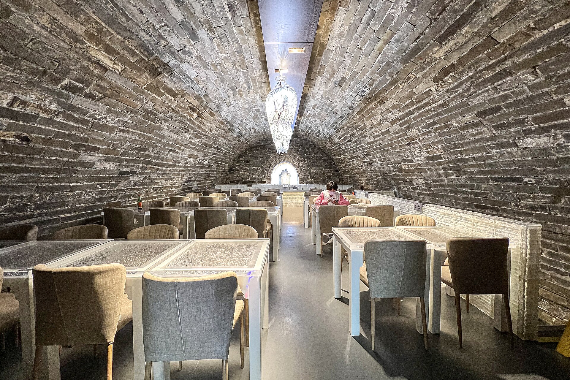 Curved brick-vaulted former ice store converted into a cafe, with modern tables and chairs.