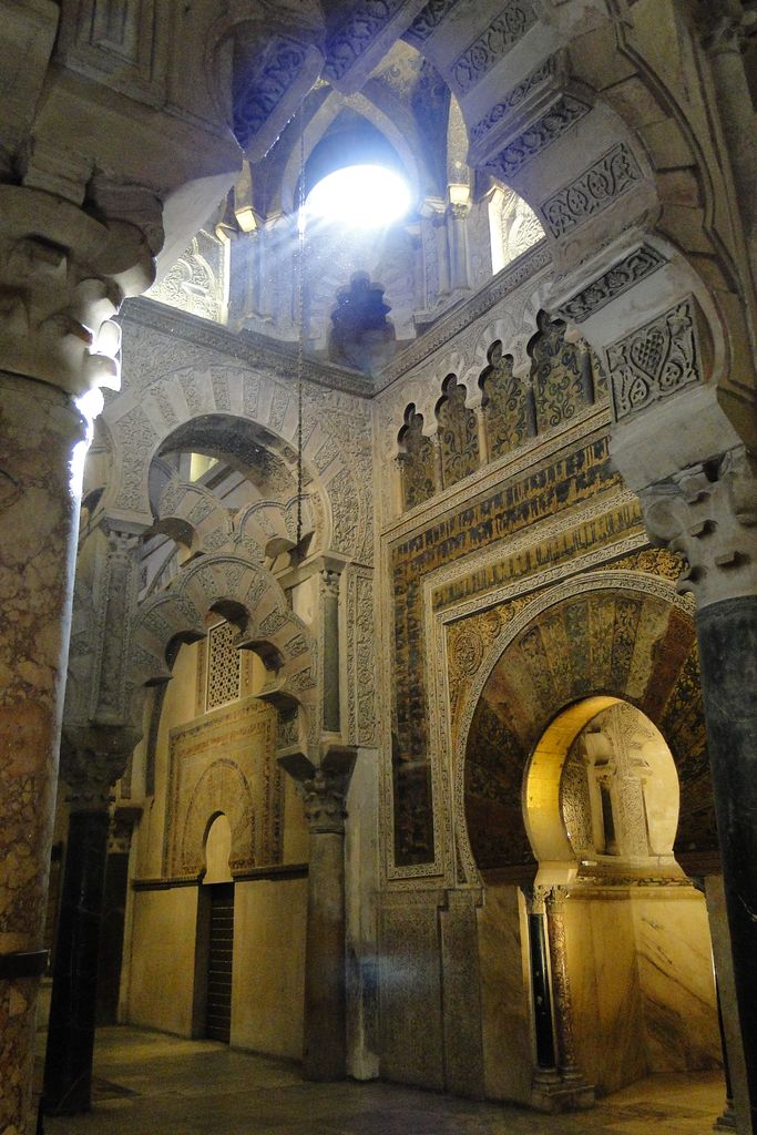 A richly patterned horseshoe portal opens into a small glowing chamber beside another doorway, beneath interlacing arches and high windows.