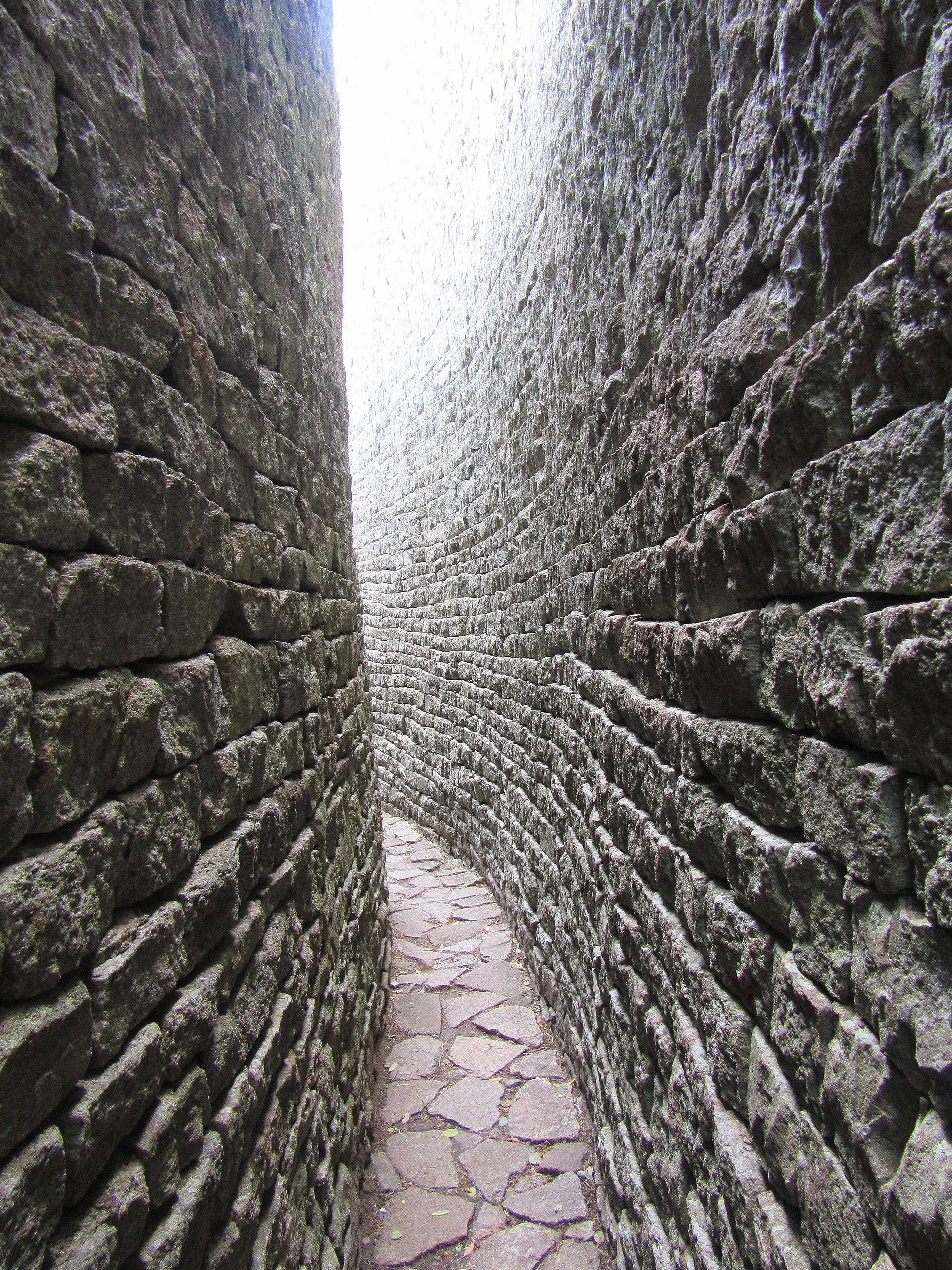 Narrow paved passage bending between two tall dry-stone walls.