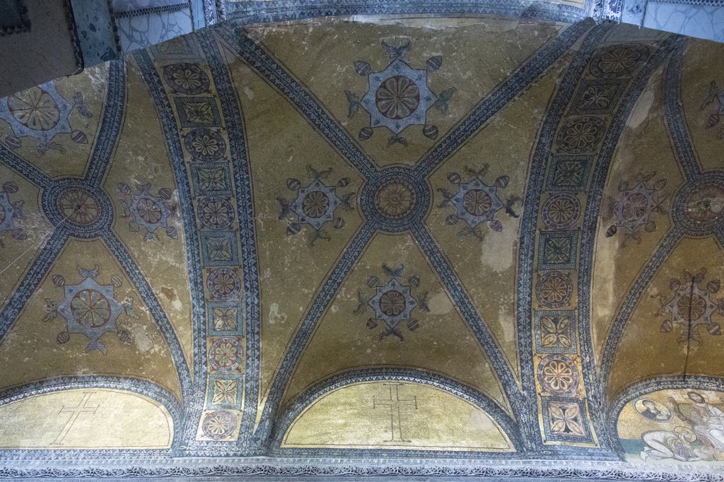 An upward view shows a row of richly patterned groin vaults with gold surfaces, floral medallions, dark decorative ribs, wear and surviving figural fragments.