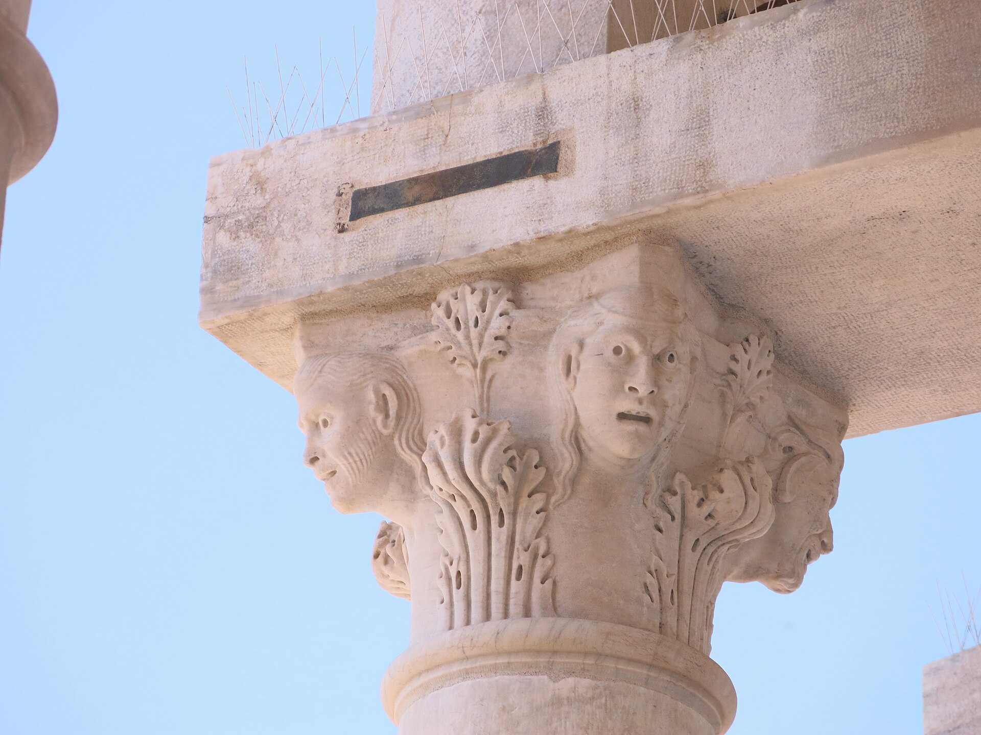 Carved stone capital high on the Leaning Tower of Pisa with foliage and human heads.