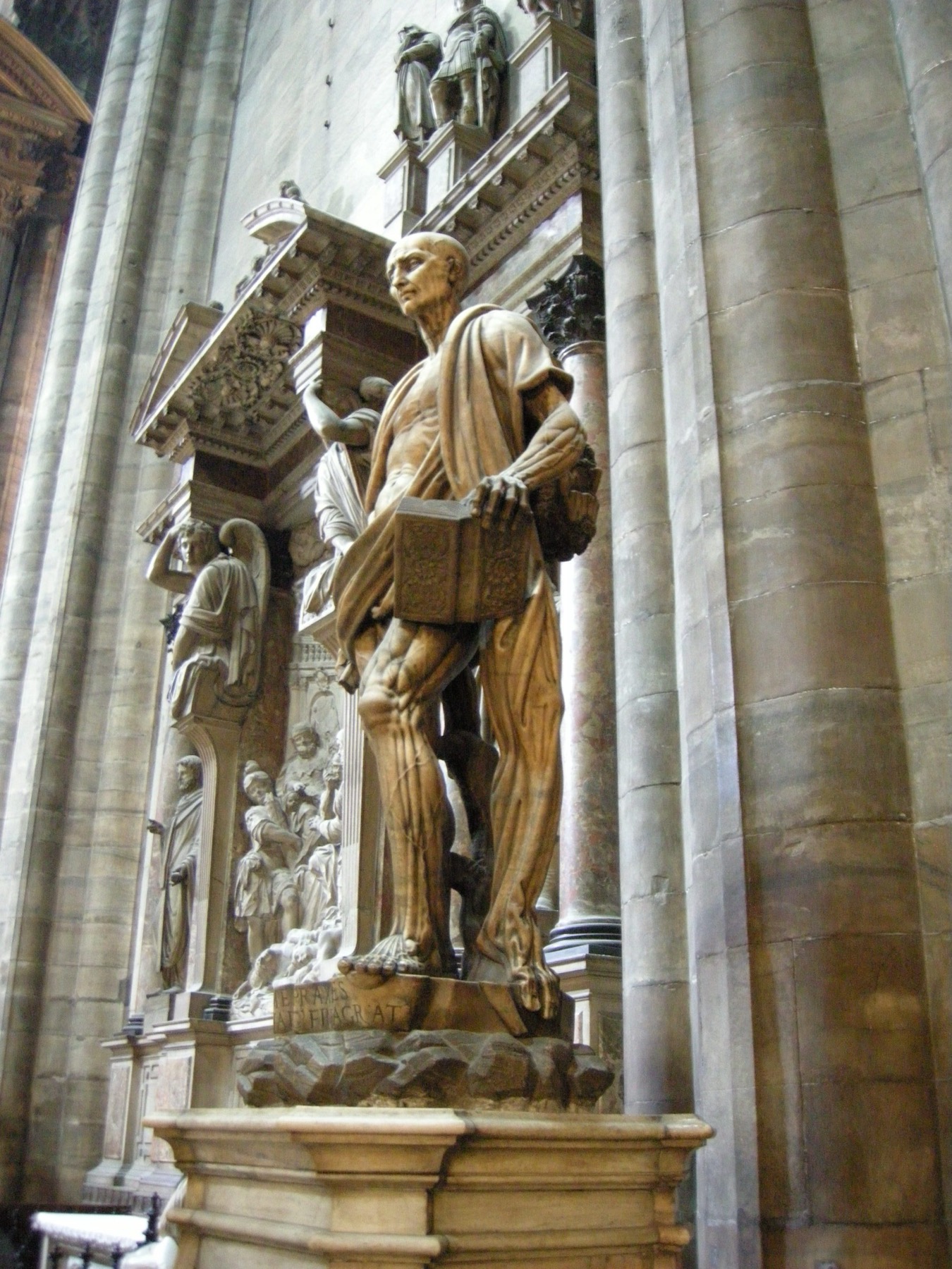 Marco d’Agrate’s marble Saint Bartholomew stands flayed, carrying his skin around his body and holding a book in Milan Cathedral.