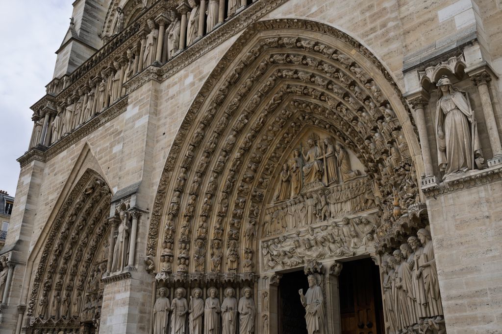 An oblique close view shows Notre-Dame's deeply carved central portal, crowded archivolts, tympanum scenes, jamb statues, an adjacent portal and part of the Gallery of Kings.