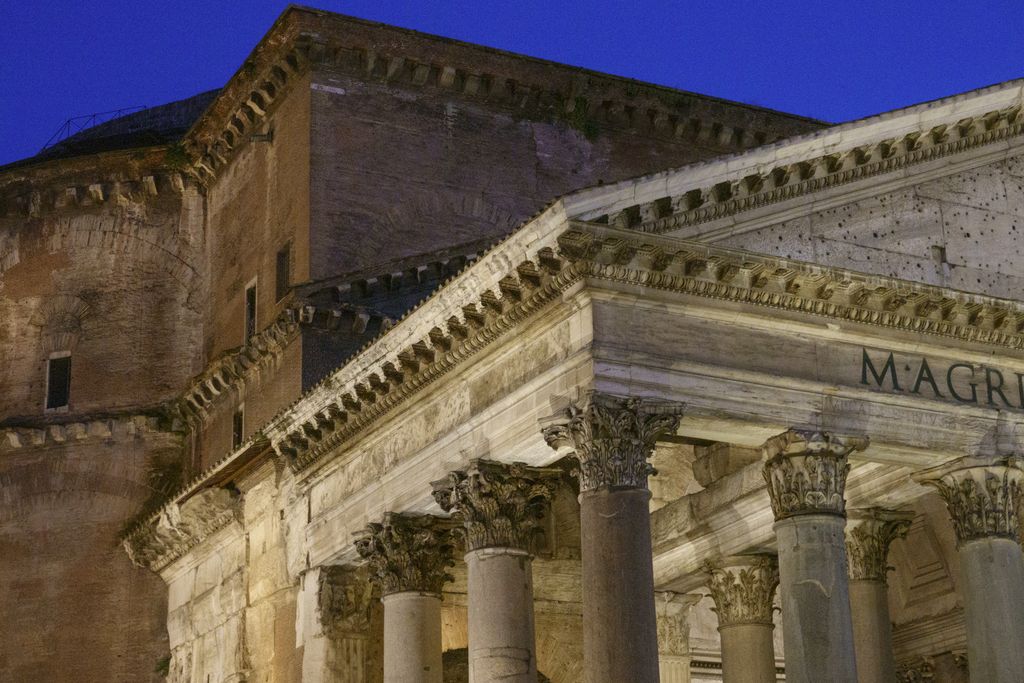 At dusk, pale Corinthian columns and the edge of the Pantheon portico overlap a dark brick cylindrical rotunda and stepped dome rising behind.