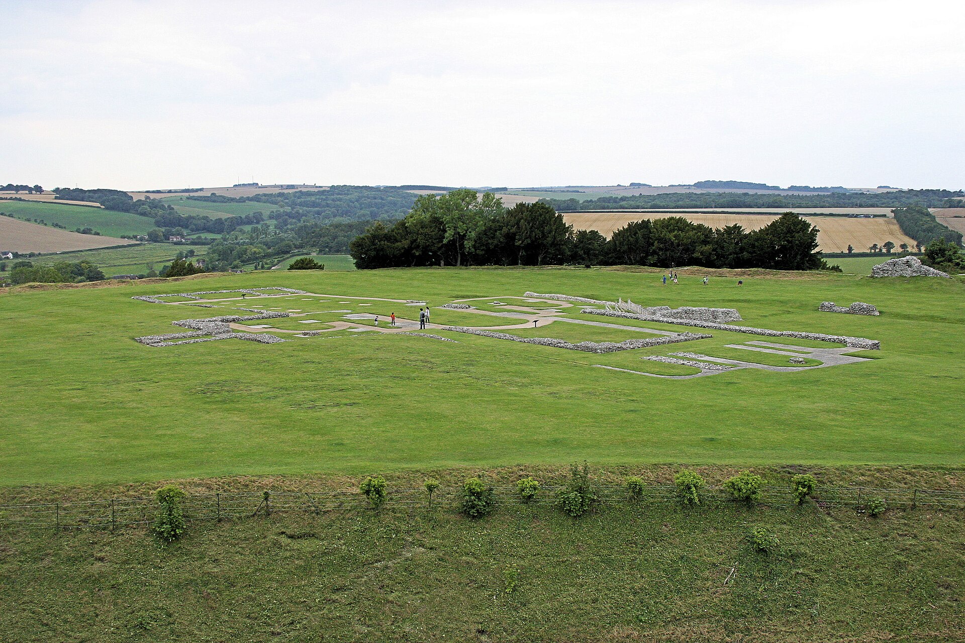 Low stone foundations outlining the former cathedral at Old Sarum on a broad grass platform above the Wiltshire countryside.
