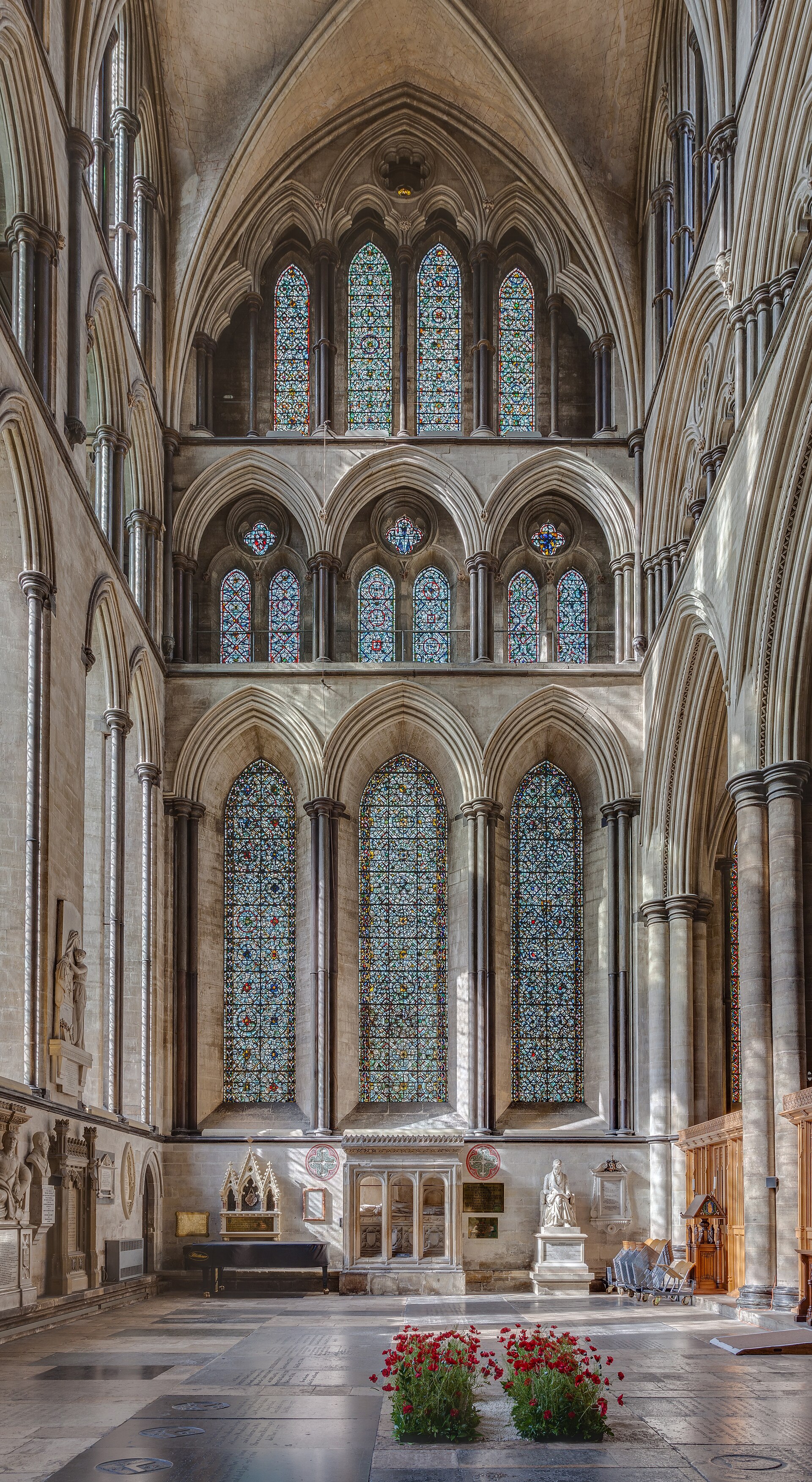 Interior wall of Salisbury Cathedral's north transept arranged in three tiers of pointed arches, patterned glass and Purbeck shafts.