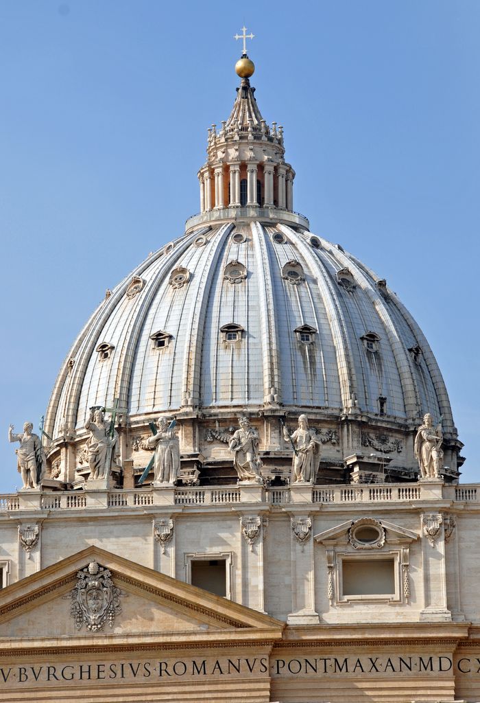 A monumental ribbed grey dome rises behind rooftop statues to an open lantern, gold sphere and cross against a blue sky.