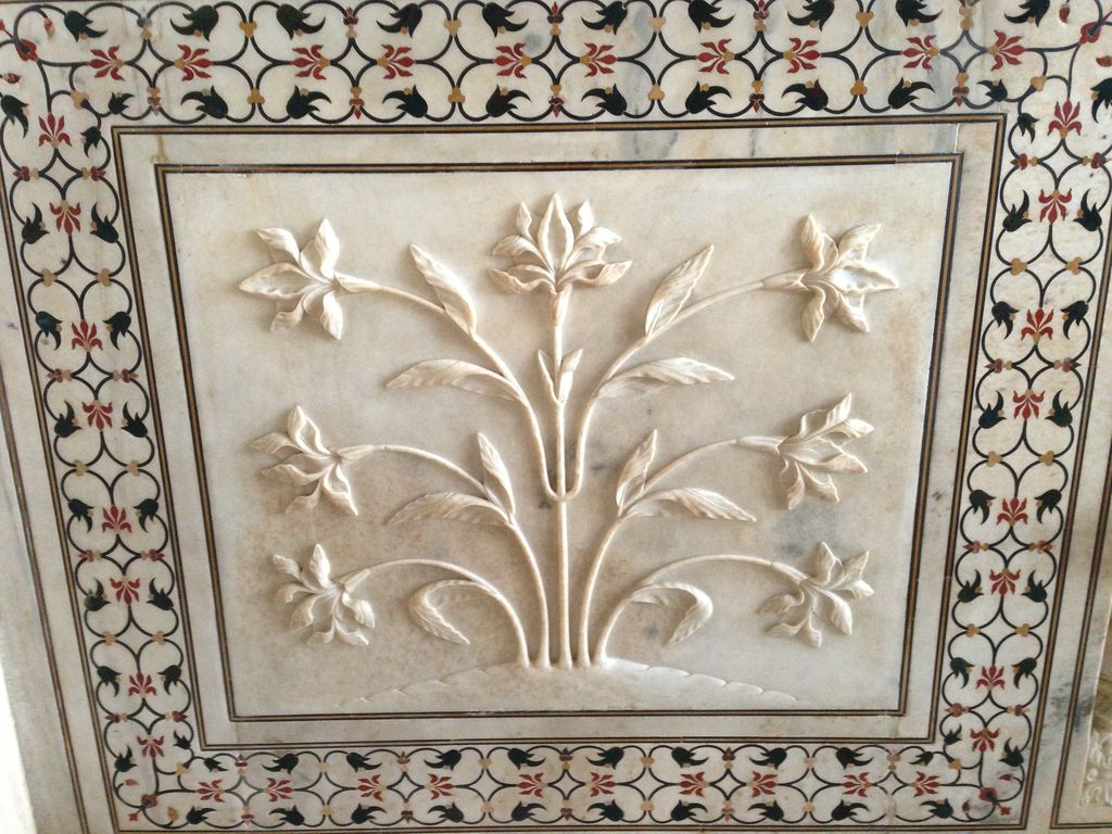 A pale marble panel bears a shallow carved flowering plant surrounded by narrow black, green, red and yellow inlaid floral borders.