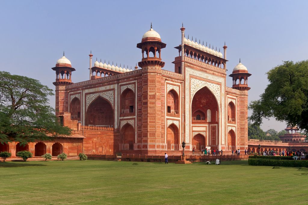 A monumental red sandstone gateway has a very tall pointed central arch, white marble inlay, smaller openings and domed corner kiosks.
