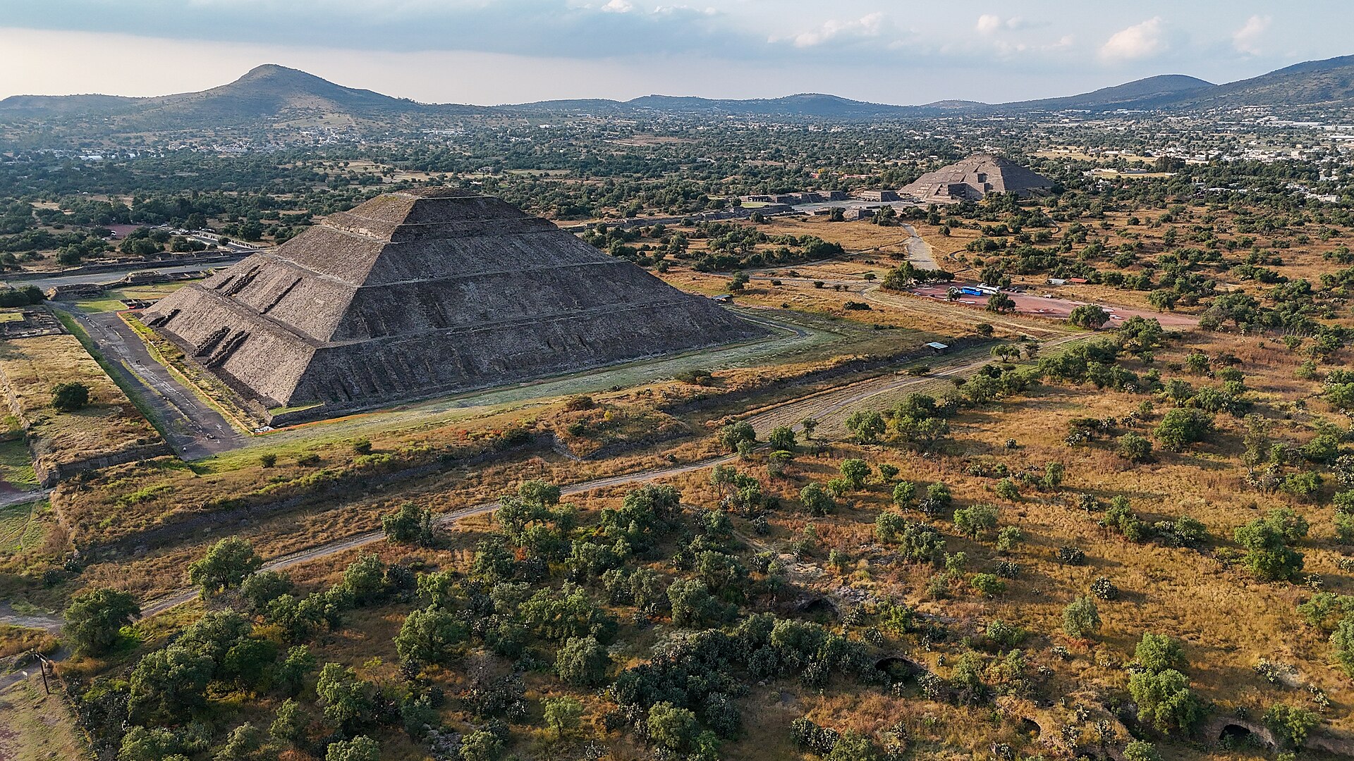 Oblique drone view of two pyramids across present-day fields, paths and nearby settlement.