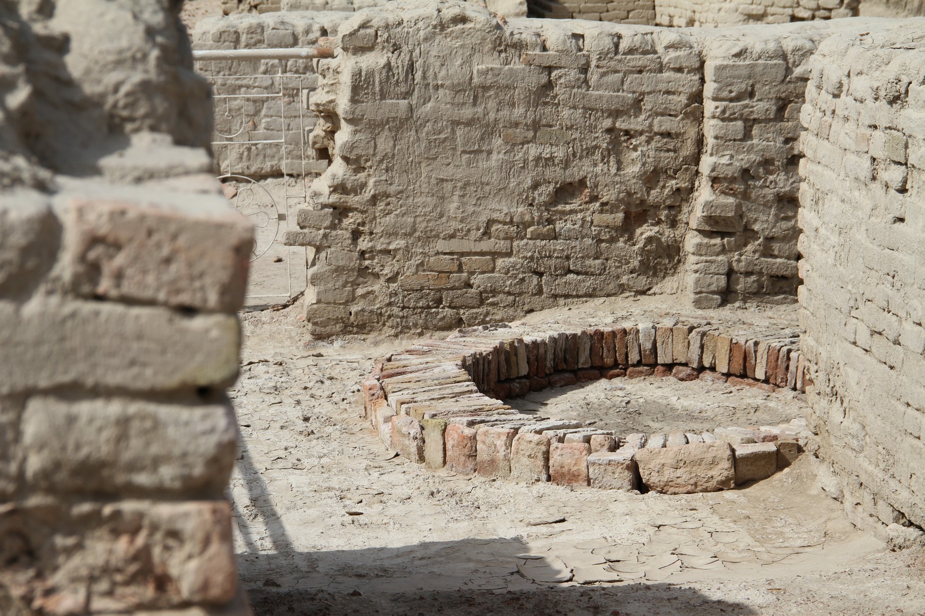 Low circular brick well lining surrounded by excavated brick walls and sandy ground.