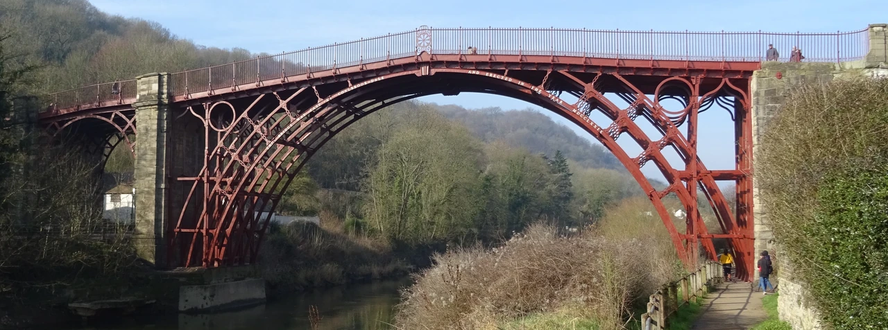 Red-painted Iron Bridge spans the Severn, with curved ribs, circular spandrel details and stone abutments.