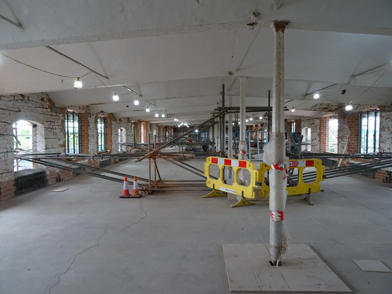 Wrapped columns and temporary supports recede through a brick-walled mill interior with large and smaller window openings.
